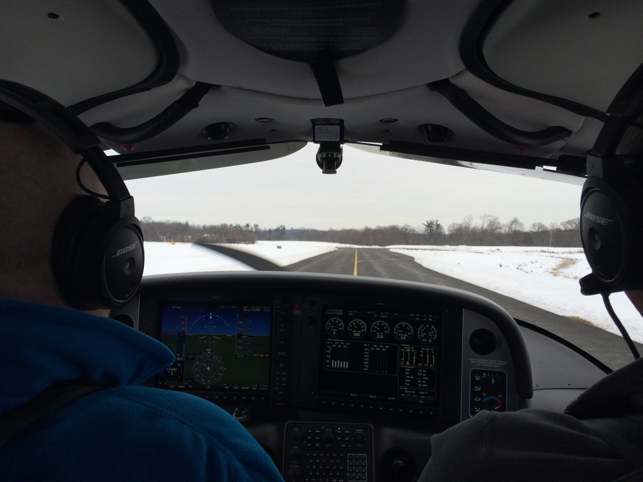 View from inside a small aircraft looking over the cockpit toward a snow-lined runway
